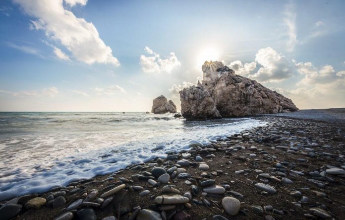 Strand met een rots waar de zon achter verdwijnt