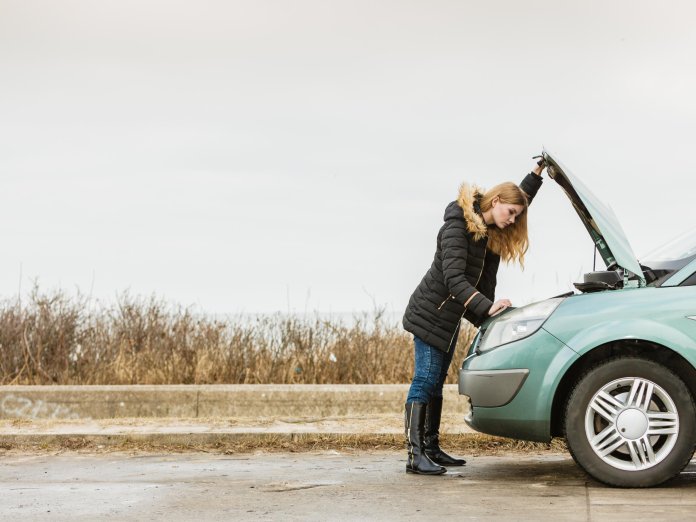 Vrouw kijkt onder motorkap autopech autobatterij