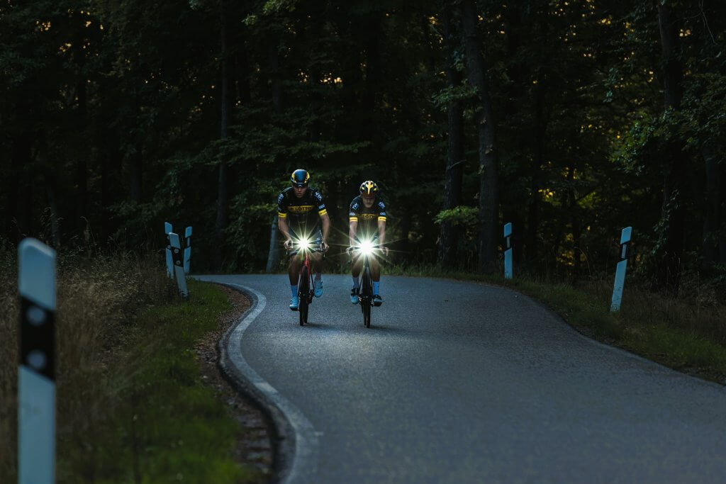 twee fietsers in het donker op een bosweg met fietsverlichting