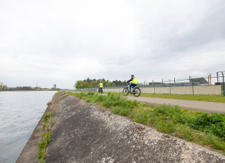 Twee fietsers met fluohesjes op een jaagpad langs een kanaal.